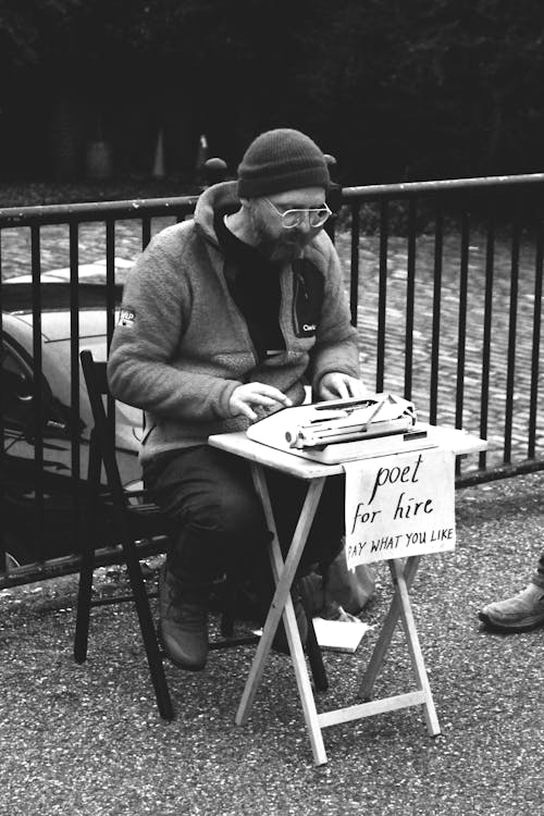 Free Street poet typing on a typewriter with a 'poet for hire' sign in a London park, UK. Stock Photo